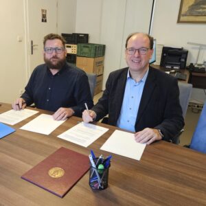 Profesor Petr Kitzler i profesor Paweł Kras siedzą przy stole, na którym leży umowa o współpracy